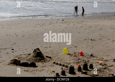 Eimer und Sandburgen am Strand mit zwei jungen waten in der Ferne Stockfoto