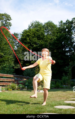 Aktive ältere Frau springt Seil im Garten Stockfoto