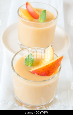 Pfirsich-Dessert in Teil Gläsern mit Pfirsich Scheiben und Minze auf weißer Holztisch, Nahaufnahme, vertikal Stockfoto