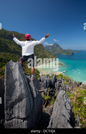 Ein Mann wirft seine Arme Eloge auf scharfen Kalkstein Türme mit Blick auf das Dorf El Nido; El Nido, Philippinen Stockfoto