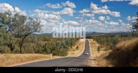 Outback / Busch / Land Straße mit Eukalyptus Bäume entweder Seite und Berge in Ferne und Auto unterwegs Queensland Australien Stockfoto