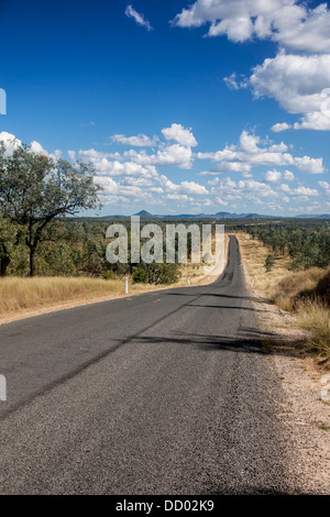 Outback / Busch / Land Straße mit Eukalyptus Bäume entweder Seite und Berge in Ferne und Auto unterwegs Queensland Australien Stockfoto