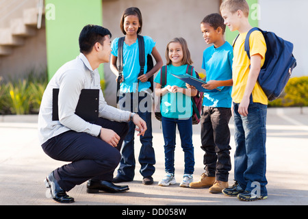 niedliche elementare Schüler außerhalb der Klassenzimmer im Gespräch mit Lehrer Stockfoto