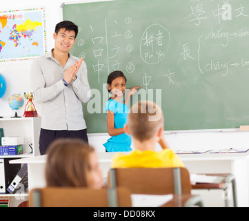 Grundschullehrerin applaudieren nach jungen Mädchen chinesische Wörter auf Tafel schrieb Stockfoto