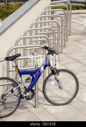 Ein blaues Fahrrad sitzt alleine in einer Zeile leer Fahrradständer. Stockfoto