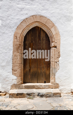 Alte hölzerne gewölbte Tür mit steinernen Torbogen und Stuck weiße Wand Stockfoto