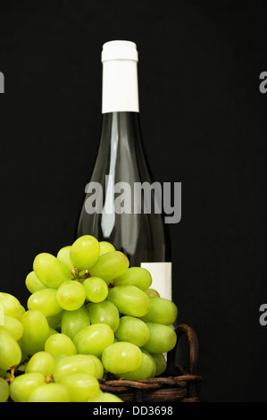 Grüne Trauben in einen Korb und eine Flasche Wein auf dunklem Hintergrund Stockfoto