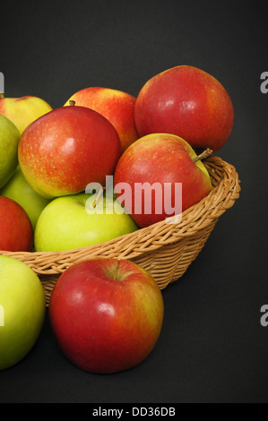 Rote und grüne Äpfel in einem Korb auf dunklem Hintergrund Stockfoto