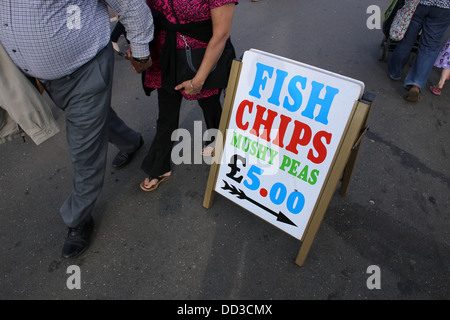 Menschen zu Fuß durch ein Straßenschild Werbung 'Fisch, Chips und Erbsenpüree £5'. Stockfoto