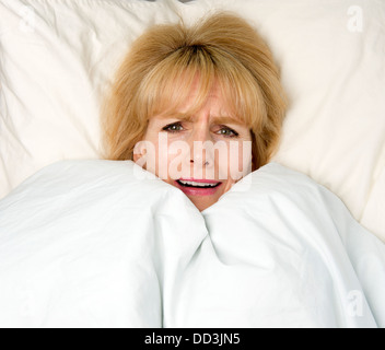 Frau, die Decke zu ziehen, um ihr Gesicht im Bett mit Ausdruck der Angst Stockfoto