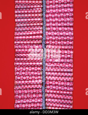 Eine Reihe von roten Feuerwerkskörper statt durch eine Sicherung. Leuchtend roten Hintergrund Stockfoto