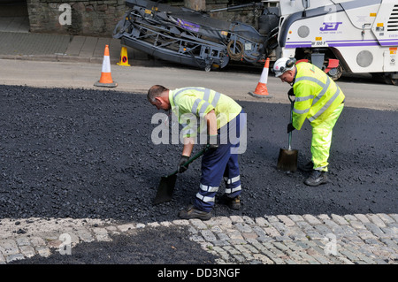 Zwei Männer mit Schaufeln sich ausbreitenden Schotter auf Asphalt während Straße Oberflächenersatz Arbeit, UK Stockfoto