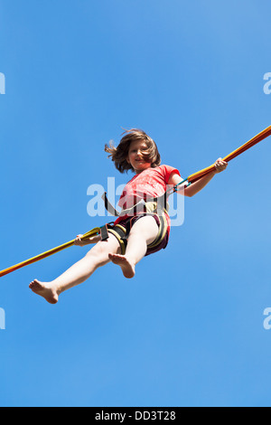 Mädchen springt am Bungee-Seil mit blauem Himmelshintergrund Stockfoto