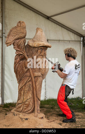 Zauberer Fantasy Märchen Elve alten Mann Eule Wanderer; Chainsaw Artist Carver in Tabley, Cheshire, Großbritannien August, 2013. Ryan Cook aus Kanada beim 9. English Open Chainsaw Carving Competition, Cheshire County Showground, Game and County Fair, Großbritannien. Die Kettensägen-Schnitzer verwenden riesige Holzstückchen, um wunderschöne Schnitzereien von altem Mann herzustellen, der 20 Meter hoch ist, mit Eule auf dem Stock. Jeder wird zu einem gefragten Kunstwerk. Holzskulptur, Sägemehl, Bildhauer, Holz, Späne, Log, professionell, arbeiten, Kunst, Künstler, Schnitt, Kettensäge, Kunstwerk aus grobem Holzstamm. Stockfoto