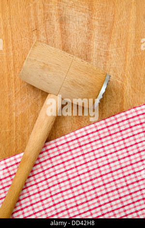 Fleischklopfer auf Holz Küchentisch, karierte Serviette im Hintergrund. Stockfoto
