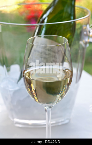 Schließen Sie die Ansicht auf Weißweinglas auf Terrasse Tisch mit Flasche und Weinkühler hinter Stockfoto