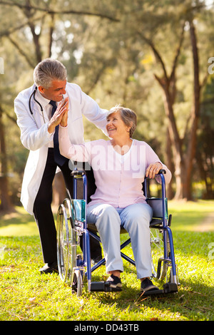 fröhlichen senior Patienten tun High-Five mit freundlichen Betreuer im freien Stockfoto