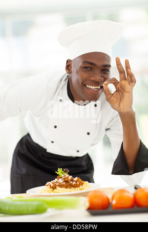 glücklich Afro amerikanische Chefkoch im weißen Uniform machen leckere Handzeichen Stockfoto