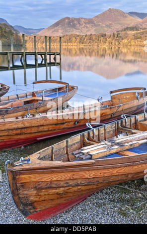 Dawn badet die Fjälls des Lake District mit ein wärmendes Licht, während die Ruderboote warten auf den neuen Tag Besucher. Stockfoto