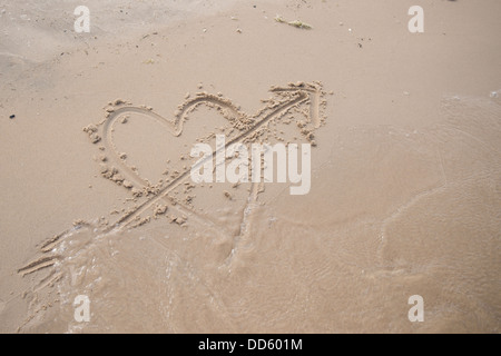 Ein Herz mit einem Pfeil durch sie an einem Strand in den Sand gezeichnet. Stockfoto