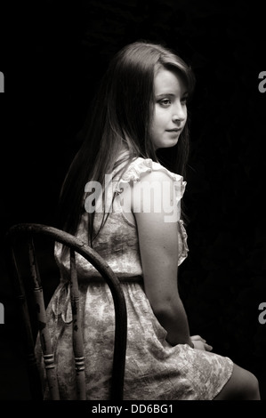 Anfang 20 junge Frau sitzt in einem antiken Farbe gesäumt Stuhl suchen Sie nachdenklich, trägt ein Kurzarm-sommerliche Kleid Stockfoto