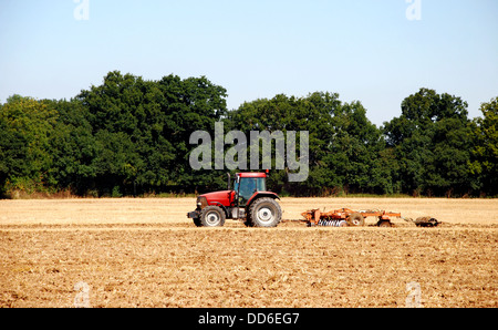 Roter Traktor und Scheibenegge brechen den Boden nach der Ernte in einem Feld-Hof - Kent, England Stockfoto