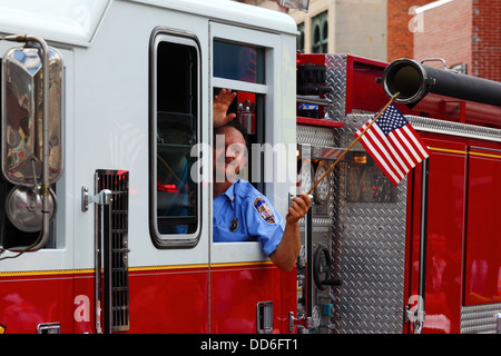 Feuerwehrmann, der amerikanische Flaggen hält, während er an den Paraden des Unabhängigkeitstages vom 4th. Juli in Catonsville, Maryland, USA, teilnimmt Stockfoto