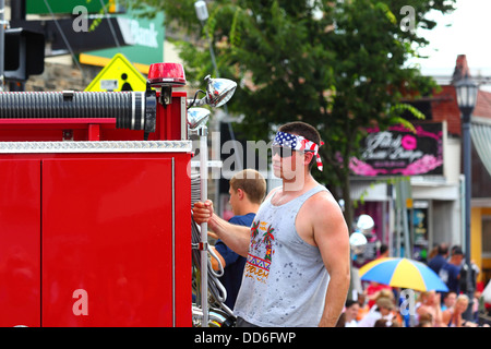 Feuerwehrmann mit einem Stirnband aus Stars and Stripes, der auf der Rückseite des Feuerwehrwagens während der Paraden zum 4. Juli in Catonsville, Maryland, USA fährt Stockfoto