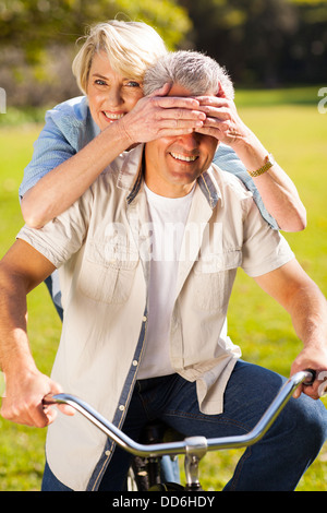 spielerische senior Frau Mannes Augen auf einem Fahrrad bedecken Stockfoto