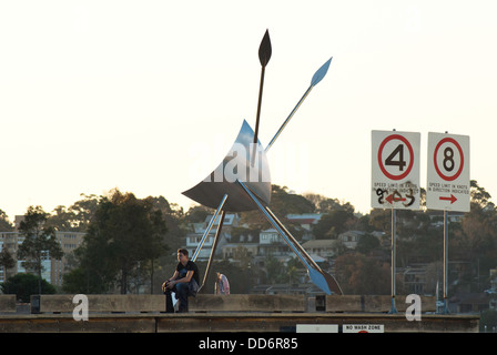 Ein junger Mann sitzt auf einem Hafen Kai in Pyrmont Sydney, als neben einem Edelstahl Skulptur der SubWharyen bezeichnet. Stockfoto