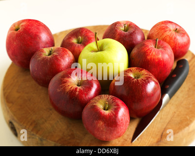 Ein paar rote Äpfel angeordnet wie ein Dreieck mit dem grünen Apfel in der Mitte und ein Messer auf dem Schneidebrett. Stockfoto