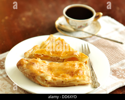 Zwei Stücke von einem Apfelkuchen und eine Gabel auf den weißen Teller mit einer Tasse Kaffee und einer Untertasse im Hintergrund Stockfoto