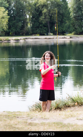 Vertikale Foto des jungen Mädchens, wir freuen uns, halten kleine Fische, die sie mit See und Bäumen im Hintergrund gefangen Stockfoto