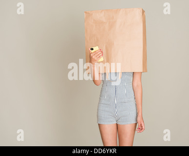Anonymer Anrufer. Junge Frau mit Papiertüte über den Kopf halten eines Handys.