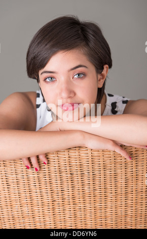 Junge, selbstbewusste Frau sitzen im Korbstuhl, Blick in die Kamera Stockfoto