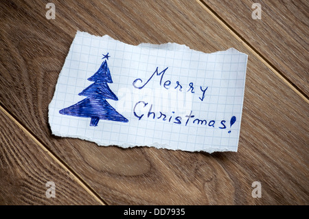 Frohe Weihnachten auf Blatt Papier, auf Holz Hintergrund geschrieben. Stockfoto