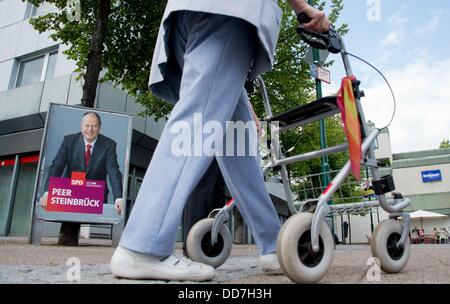 Ein Wahlplakat der Kanzlerkandidat der SPD, Peer Steinbrück, neben einer alten Frau zu Fuß entlang der Straße mit einer fahrbaren Gehhilfe in Seelze, Deutschland, 20. August 2013. Foto: Julian Stratenschulte Stockfoto