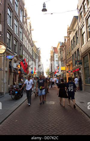 Eine belebte Straße von Amsterdam in der Abenddämmerung mit ikonischen Fahrräder geparkt entlang der Seite, während Menschen Geschäfte, Cafés und Bars besuchen. Stockfoto