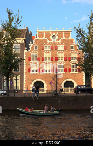 Ikonische niederländische Gebäude in der Dämmerung mit Menschen neben dem Kanal Bootstouren und sightseeing in Amsterdam. Stockfoto