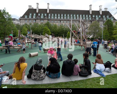 Gemischte Kulturen Familien Eltern Kinder Kinder muslimische Mädchen Jungen spielen auf einem Spielplatz in der Nähe des London Eye Southbank London England Großbritannien KATHY DEWITT Stockfoto