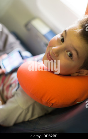 Kind mit seiner Spieler und Orange Nackenkissen im Flugzeug reisen Stockfoto