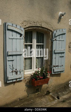 Typische blaue Fensterläden mit französischen Bögen und Blumen in der Fensterbox Stockfoto