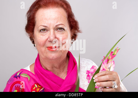 Red Hair Senior Woman mit Gladiolen Blume suchen bestimmt. Stockfoto