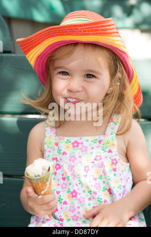 Süßes kleines blondes Mädchen in einem Strohhut Essen ihr Eis in der Sommersonne Stockfoto