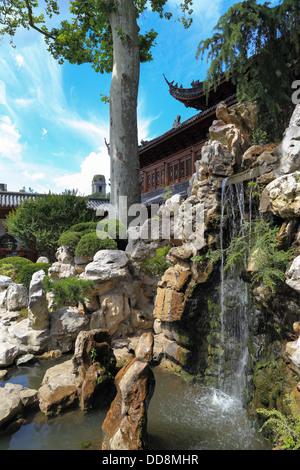 Chinesischer Tempel in einem schönen Garten mit einem Wasserfall, Bäumen und Steinen. blauer Himmel. Niemand Stockfoto