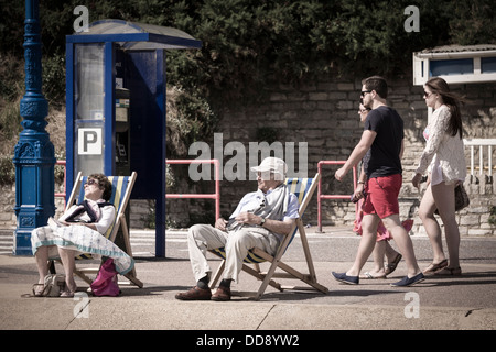 Ein paar sitzen in Liegestühlen am Meer in Bournemouth, England Stockfoto