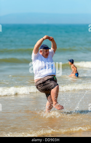 Ein großer Mann tanzt in der Brandung am Strand von Bournemouth in England. Stockfoto