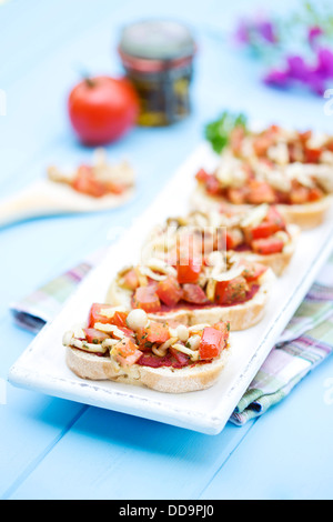 Teller mit Bruschetta mit Tomaten, weiße Shimeji Pilze, Kräuter und Olivenöl auf Holztisch, Nahaufnahme Stockfoto