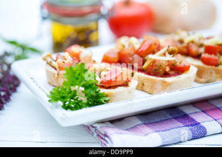 Teller mit Bruschetta mit Tomaten, weiße Shimeji Pilze, Kräuter und Olivenöl auf Holztisch, Nahaufnahme Stockfoto