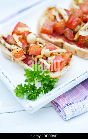 Teller mit Bruschetta mit Tomaten, weiße Shimeji Pilze und Kräuter auf Holztisch, Nahaufnahme Stockfoto